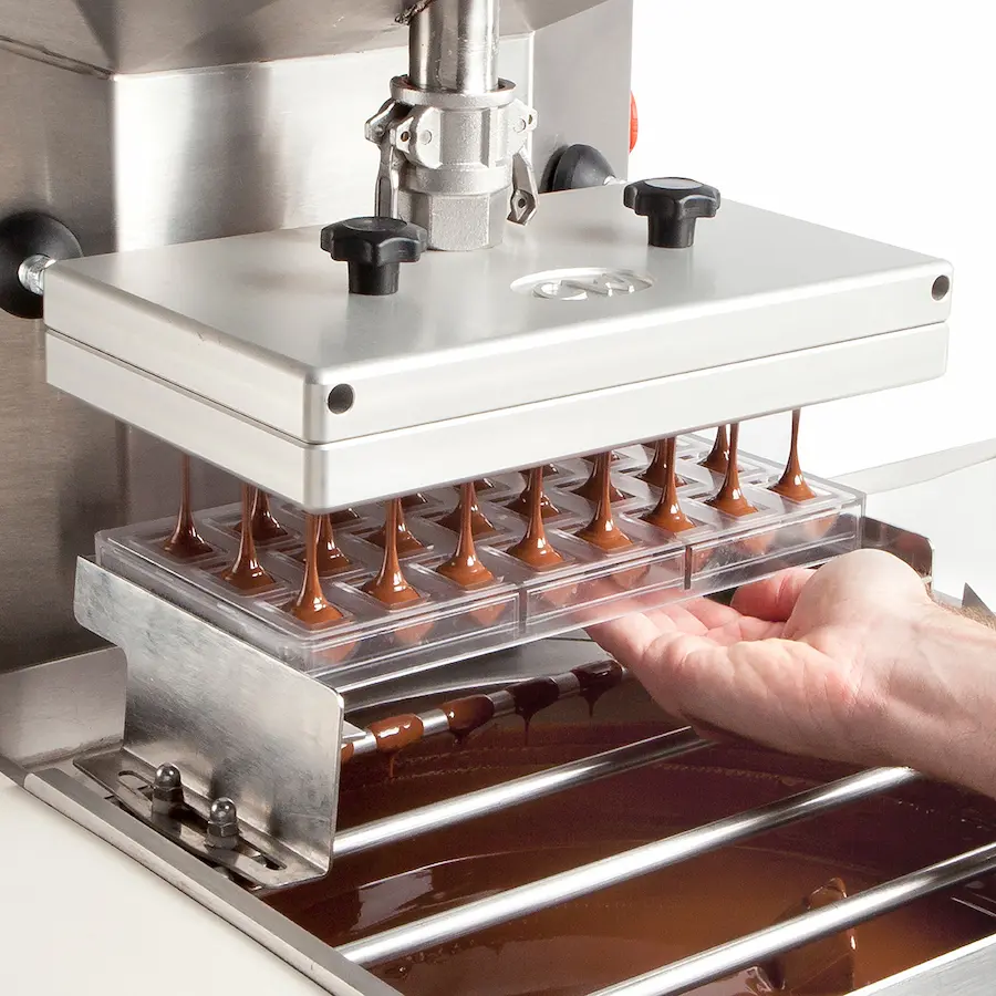 Templadora depositando chocolate en moldes de policarbonato