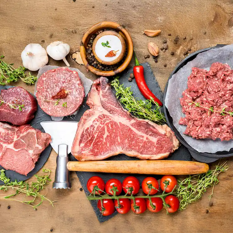 Cortes de carne fresca y carne molida sobre tabla, con ajo, pimienta y tomates